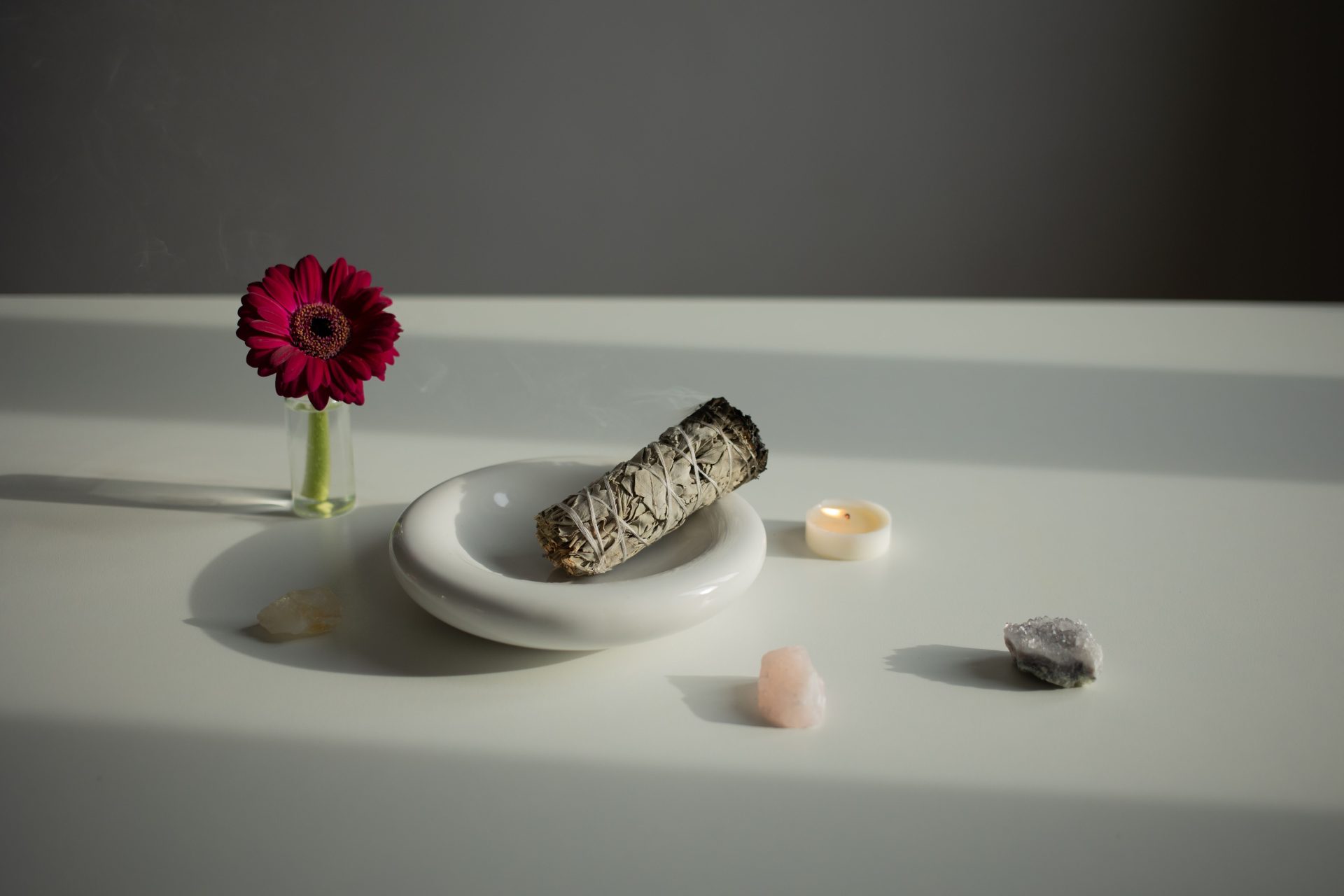 Elegant arrangement of aromatherapy essentials with sage, gerbera, and crystals on a white surface.