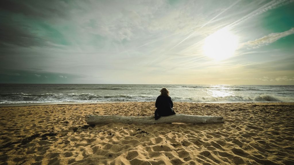 Person sitting on log facing the ocean waves.